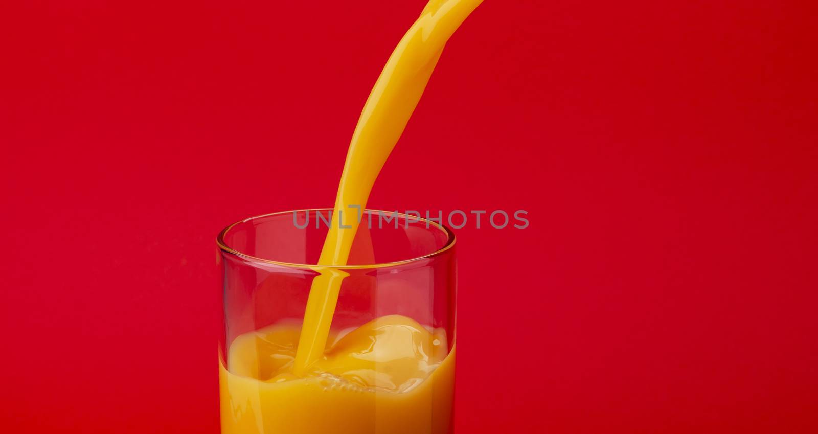 Orange juice pouring into glass, isolated on red colour background, with copy space, healthy drink concept, close-up