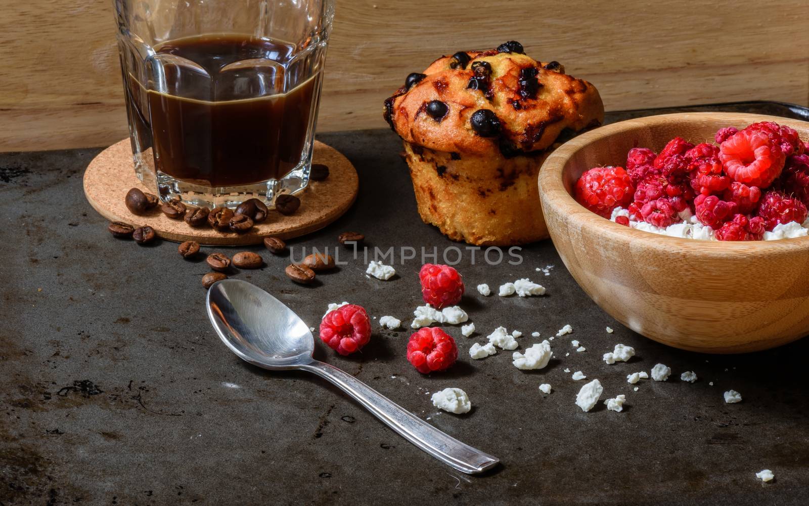 Cottage cheese with raspberries, coffee in a cup and blueberry muffin for breakfast with scattered berries, grains of curd and coffee beans