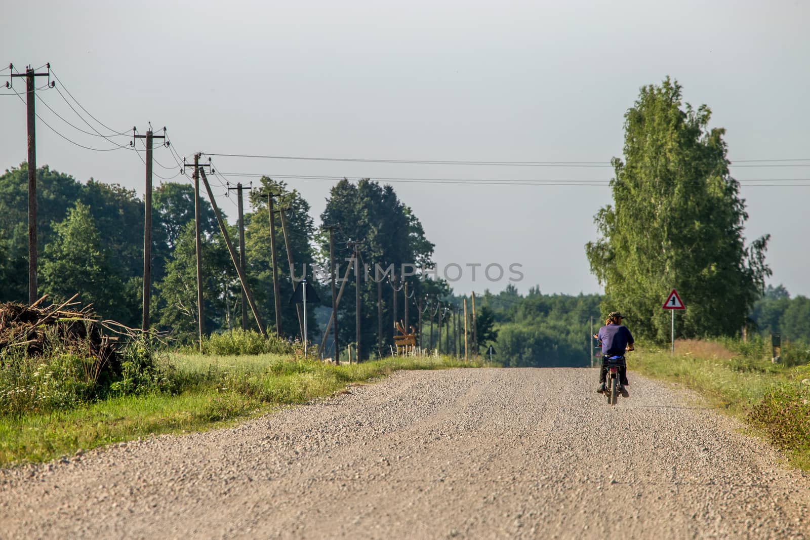 Summer landscape with road, trees and blue sky. Man ride to the moped on countryside road. Rural road, cornfield, wood and cloudy blue sky. Classic rural landscape in Latvia.