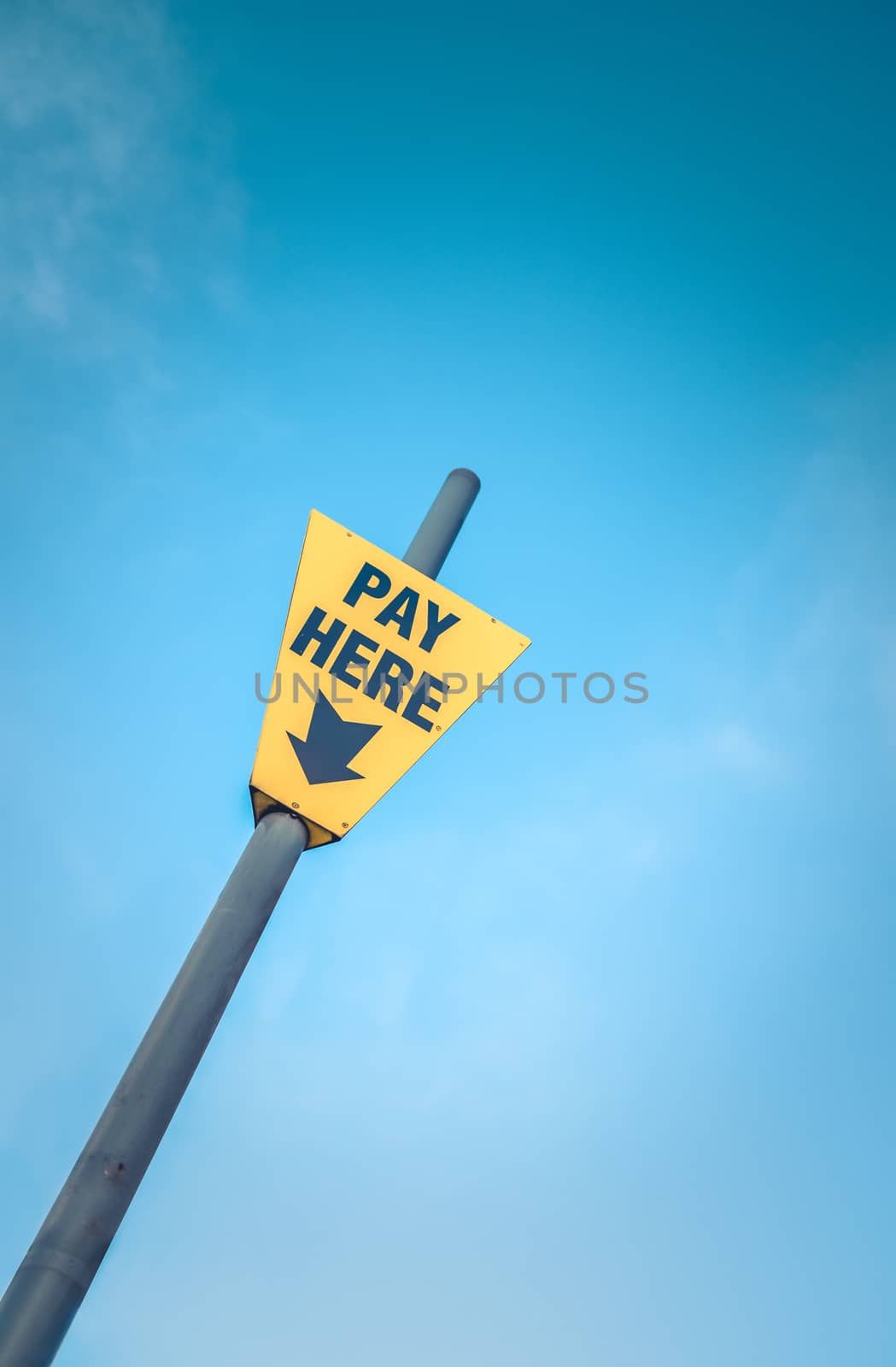 Conceptual Image Of A Bright Yellow Pay Here Sign Against A Blue Sky With Copy Space