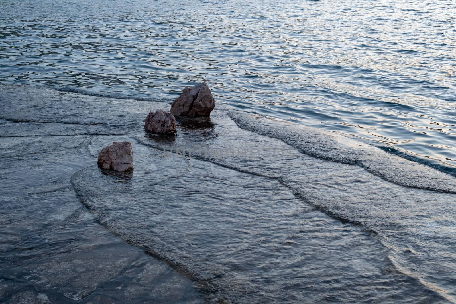 Beach after sunset, small waves, ripples hitting beach with rocks, flushing over, three rocks in row overlapping, tranquil scene