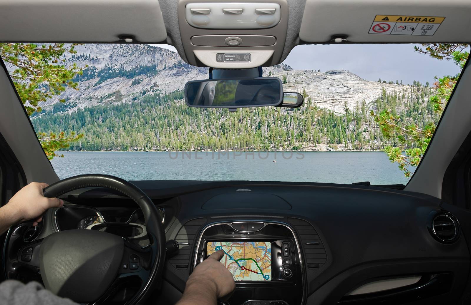 Driving a car while using the touch screen of a GPS navigation system towards a beautiful green valley and lake in Yosemite National Park, California, USA