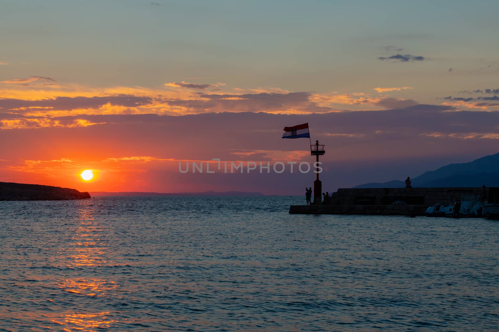 Croatian flag flying in wind at sunset in harbor, all people silhuetted and unrecognizable