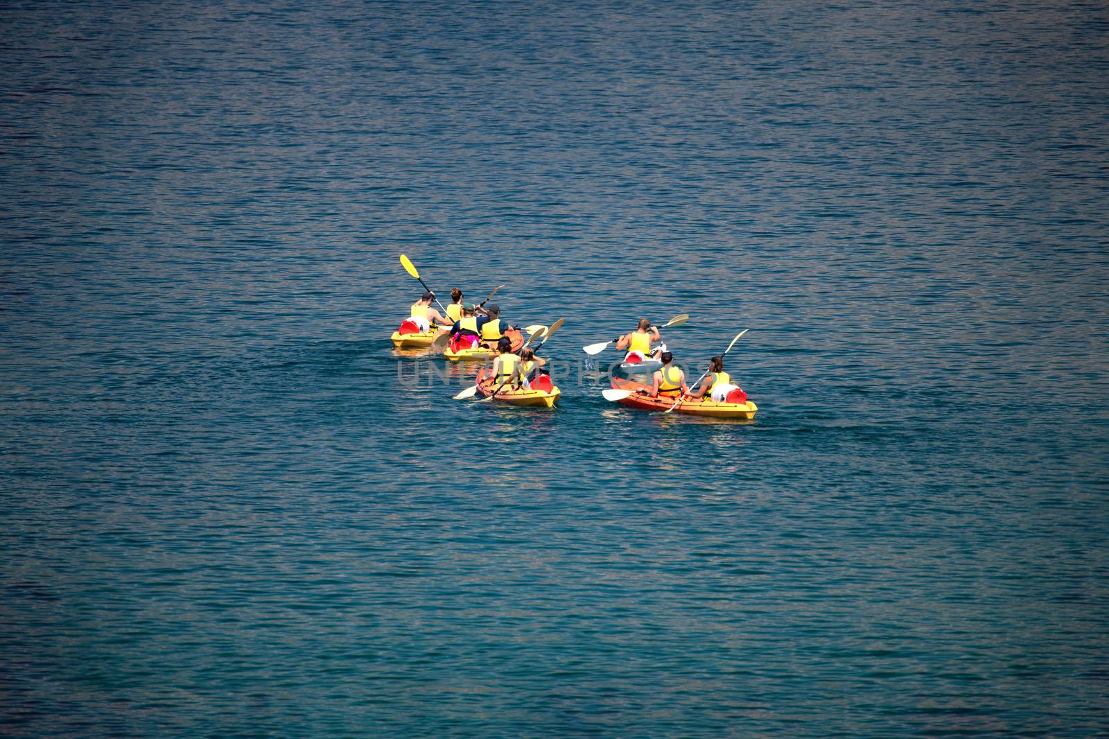 Mixed group of people, facing away, unrecogizable, canoeing at sea, vacation sport recreation, holiday outdoor activity