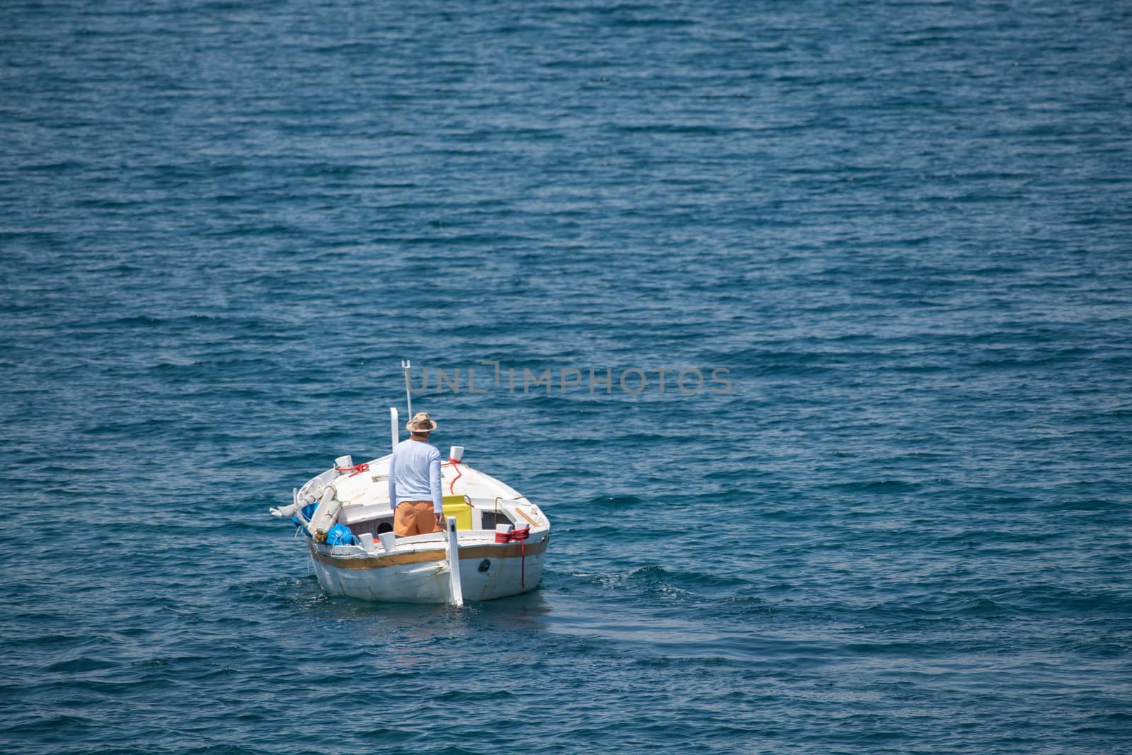 Fisherman in traditional wooden boat at sea, facing awaz from viewer, going out to sea, daylight, authentic and unstaged, mediterranean style, could be Italy, Greece, Croatia or Adriatic sea