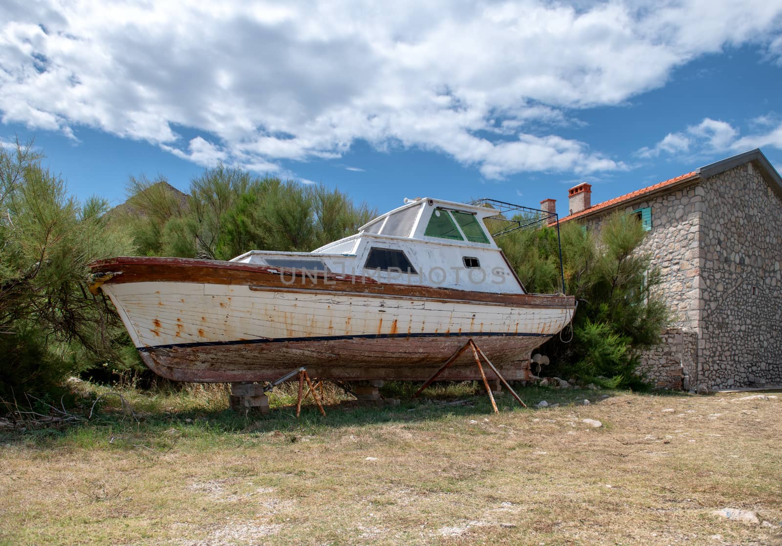 Abandoned boat on shore stone house in background by asafaric