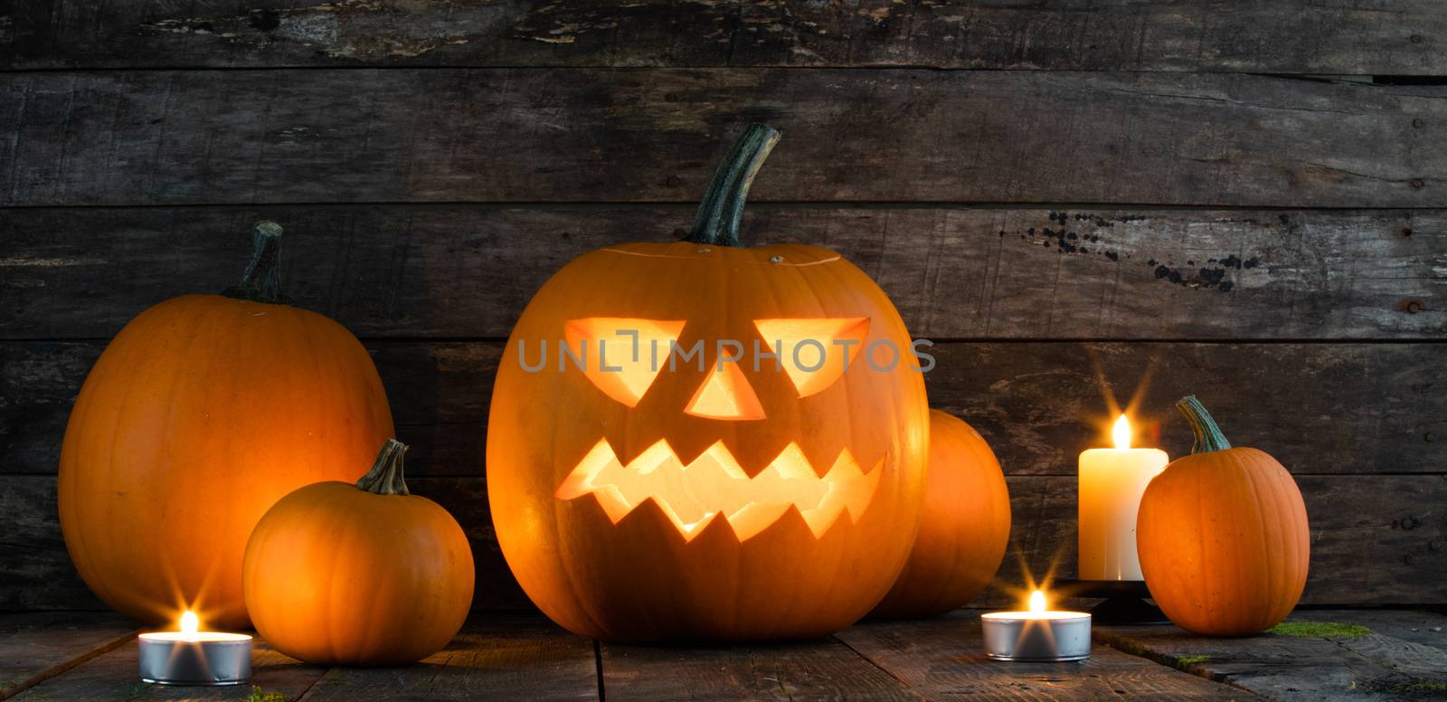 Halloween pumpkin head jack o lantern and candles on wooden background