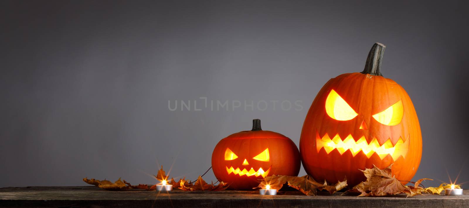Halloween pumpkins head jack o lantern and dry maple leaves on wooden background