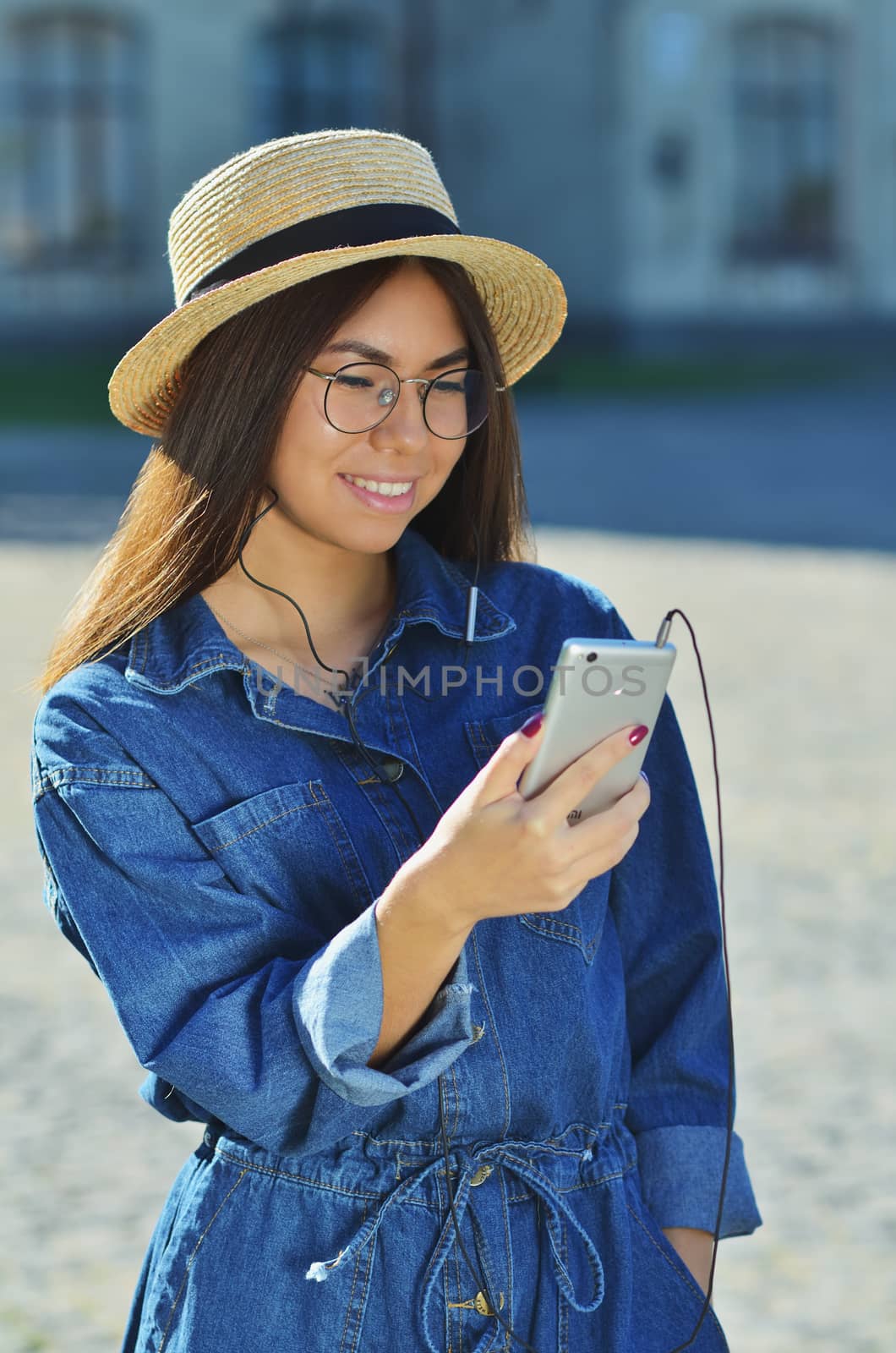 An attractive young Asian woman wearing sunglasses and a denim suit standing outside with a silver-colored phone