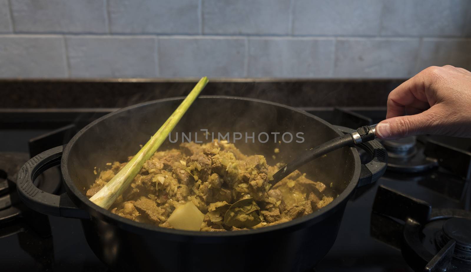 woman hand stirs in a pan on the gas stove with indonesian rendang, a stew with beef