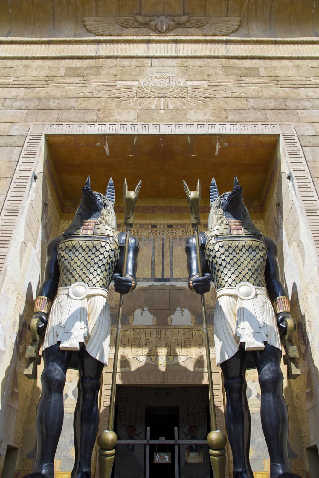 Two huge statues of the Egyptian god Anubis - the god of the afterlife with batons in their hands guard the entrance to the building. Bottom view.