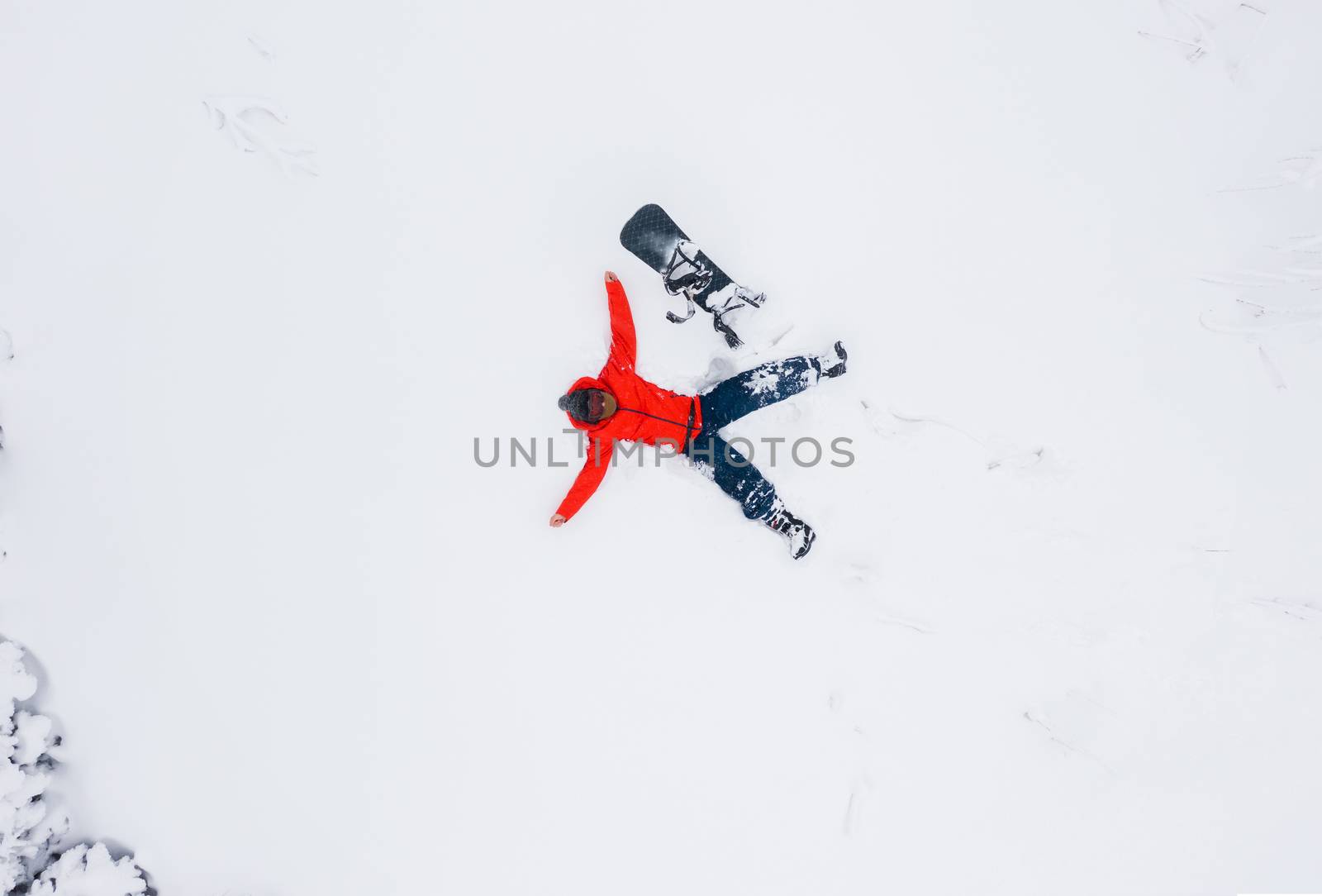 Aerial view of a man who lies in the snow with his arms outstretched next to his snowboard