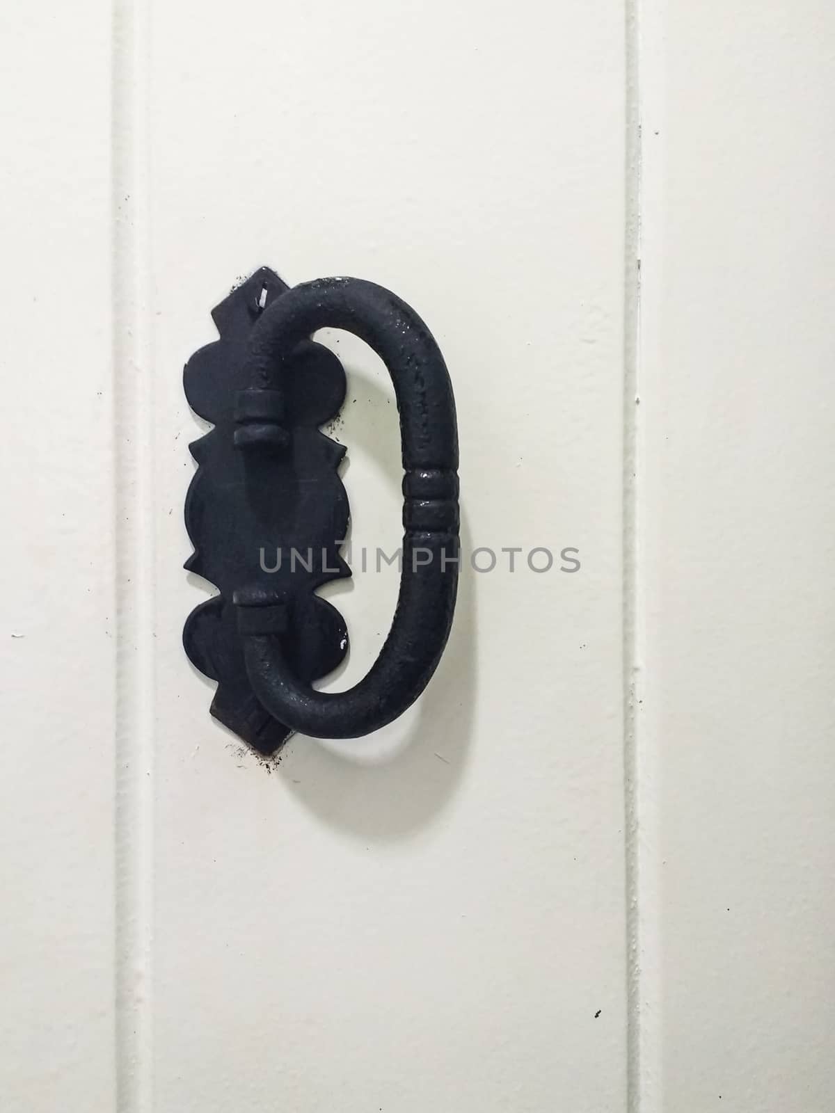 Old door handle in black metal with reliefs, on white door.