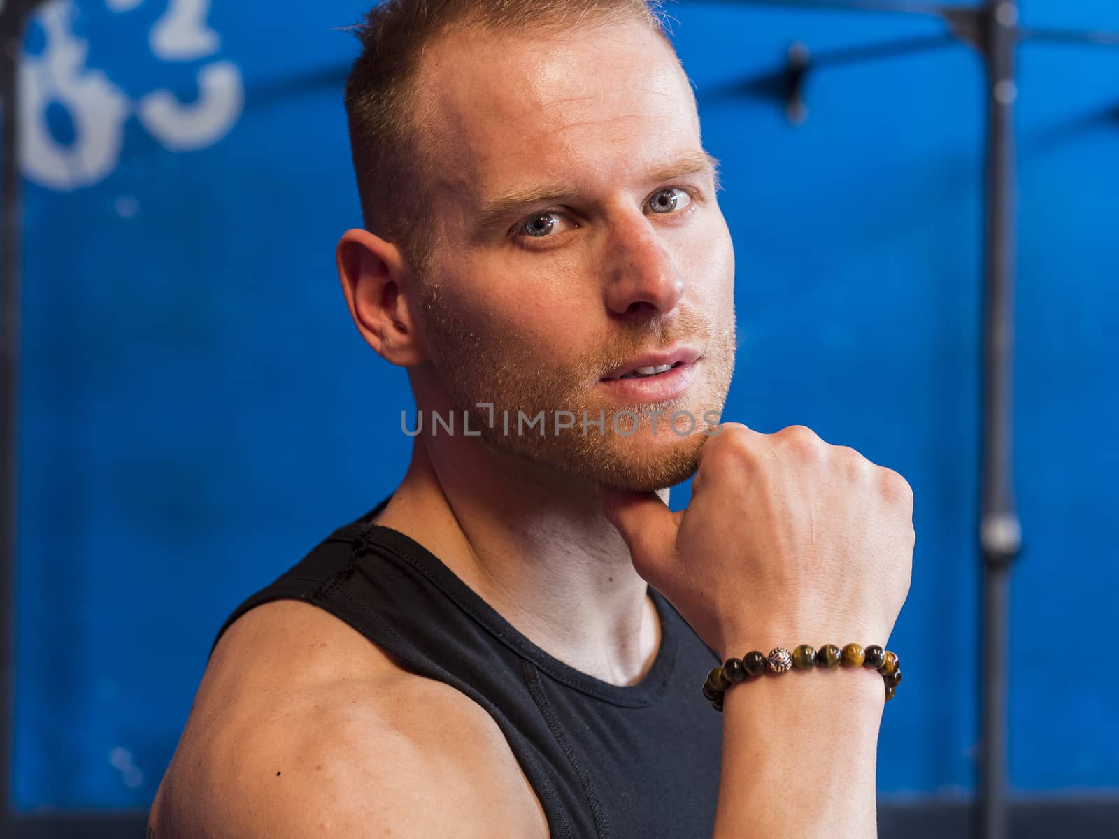 Attractive young man indoors wearing a tanktop and beaded bracelets
