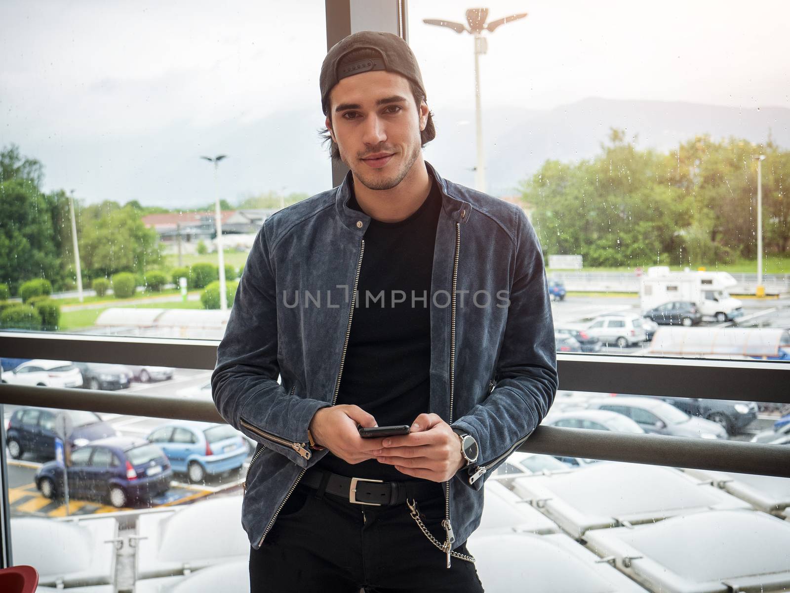 Attractive young man indoors wearing a denim jacket and baseball cap, reversed