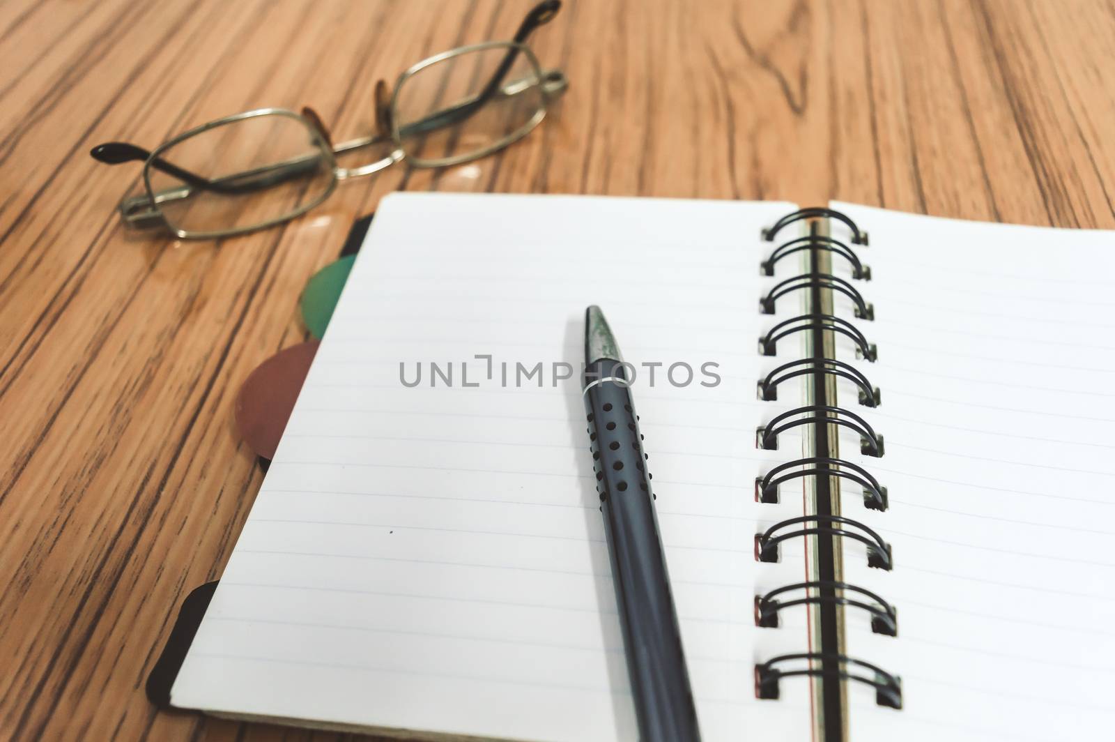 Desk with open notebook with blank pages, eye glasses and a pen. Business still life concept with office stuff on table. Education, working and planning concept. Selective focus with shallow DOF.