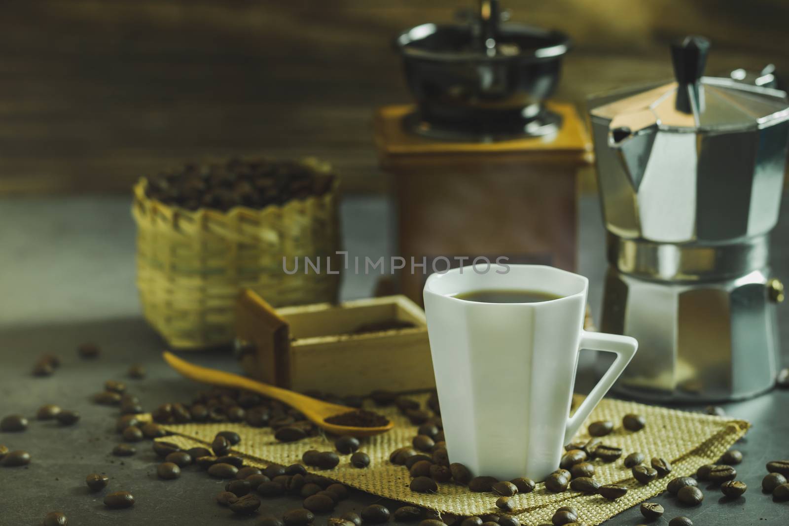 Brew black coffee in a white cup and morning lighting. Roasted coffee beans in a bamboo basket and wooden spoon. Vintage coffee grinder and moka pot. Concept of coffee time in morning or start the new day.