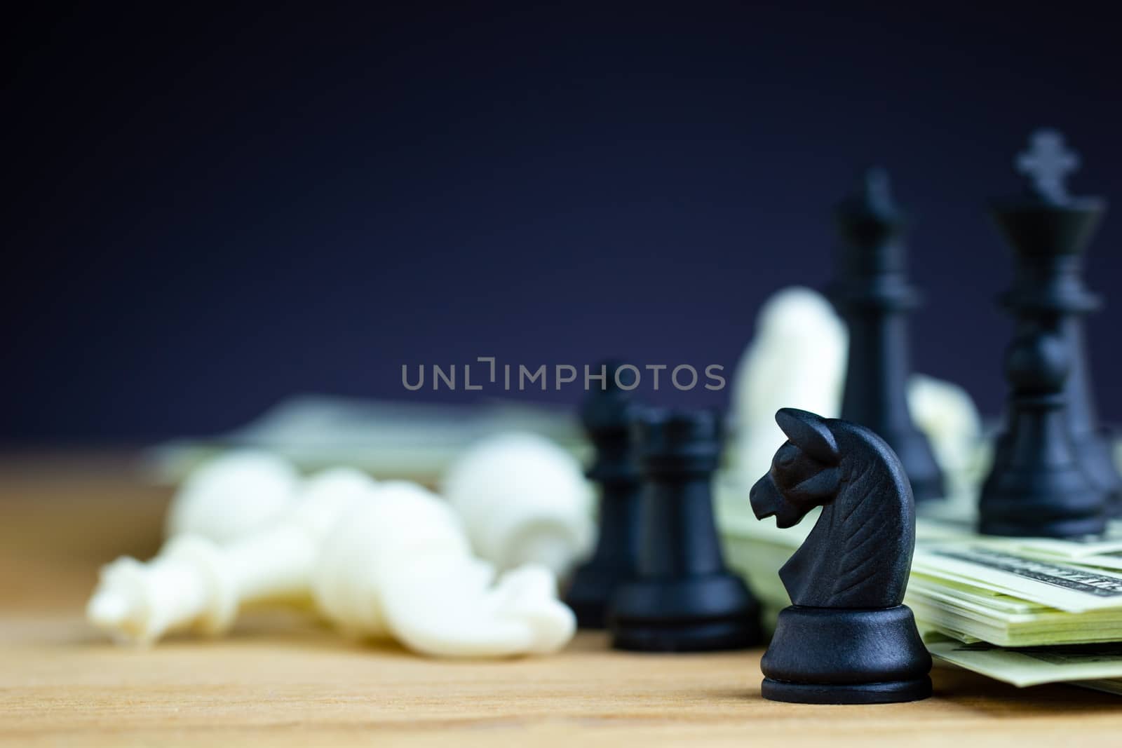 Black chess stands on top of dollar banknotes and wooden tables with white chess is falling. Concept of win or advantage and defeat of business competitors