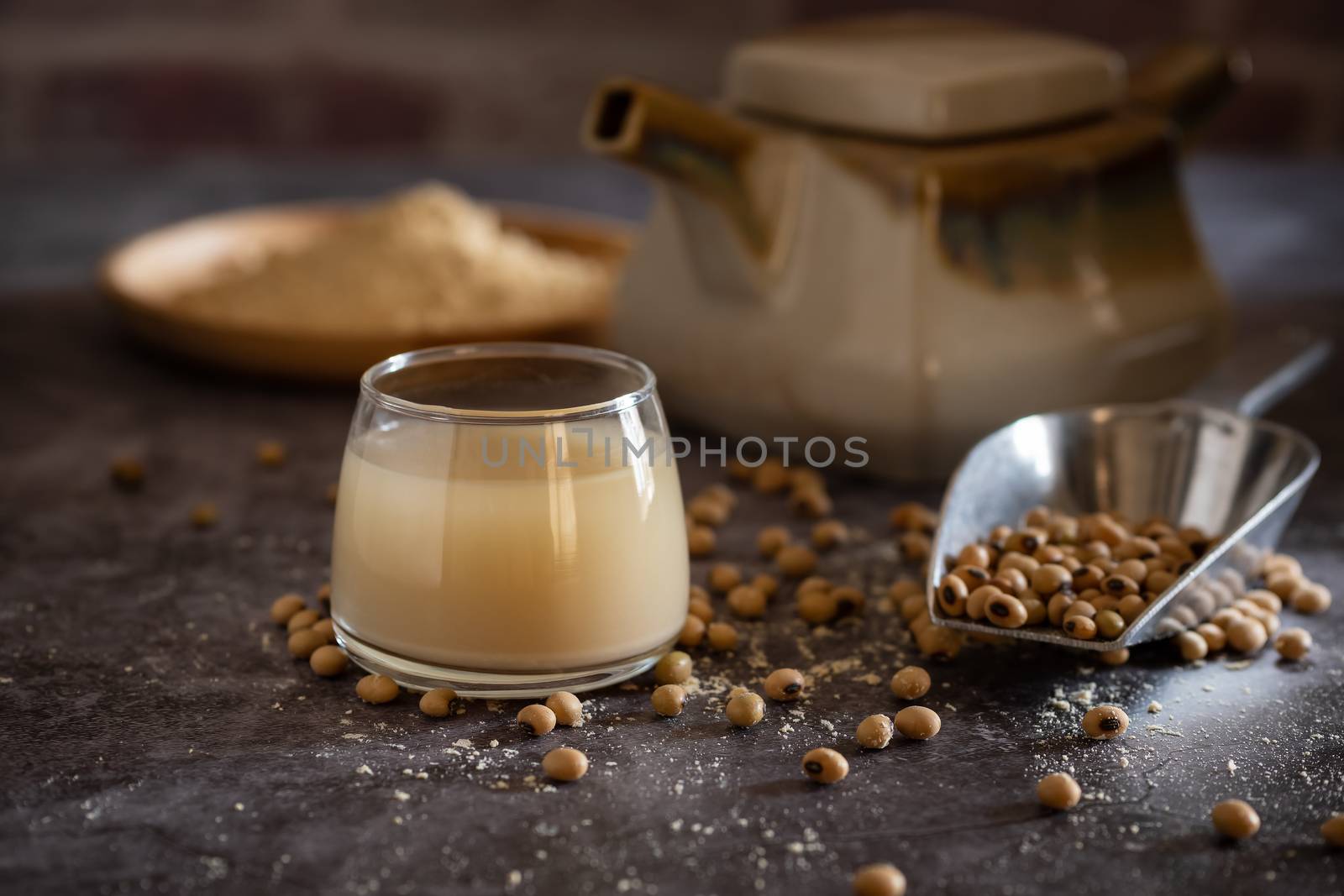 Soymilk in the glass and the kettle is placed beside. Soybean powder is crushed in a wooden dish and has scattered soy beans on the table in morning light.