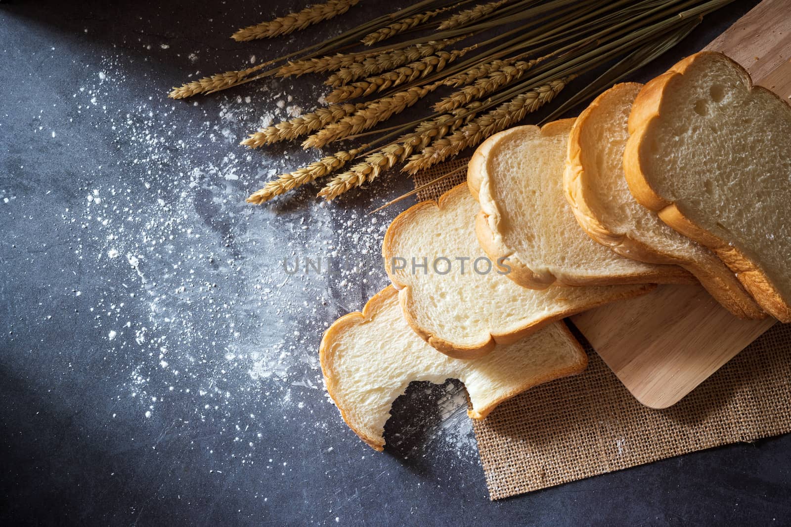 Bread on a wooden cutting board and the wheat grains placed beside With wheat flour scattered. Breakfast on the marble table and morning sunlight.