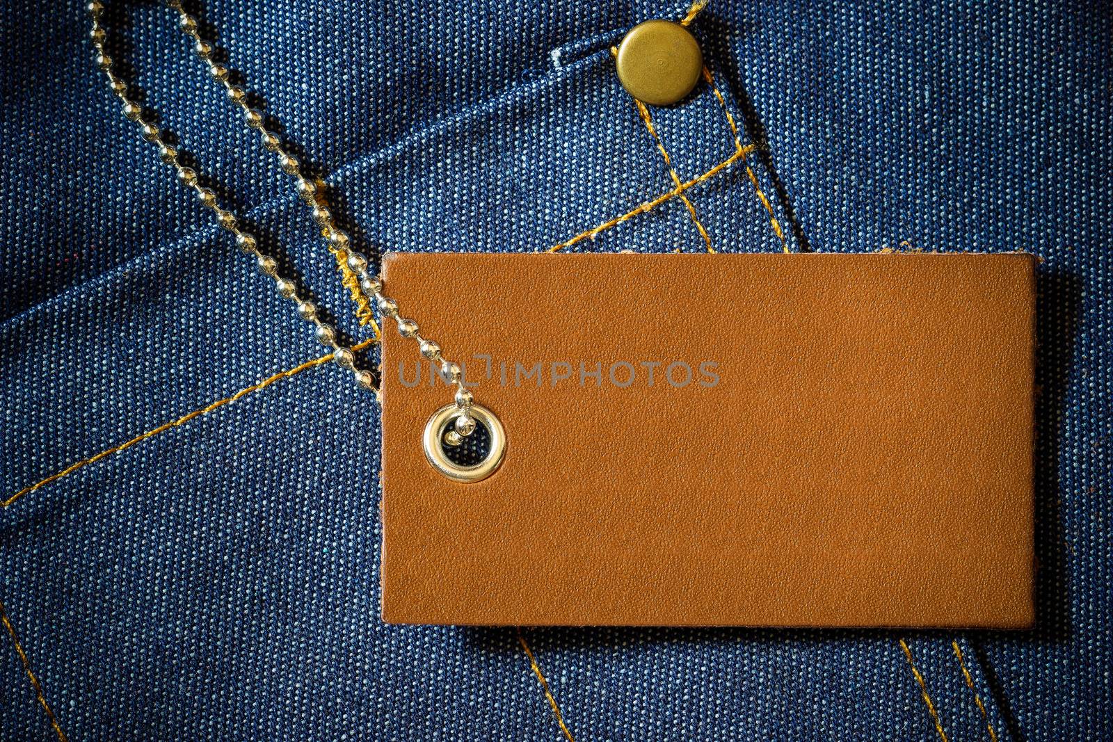 Leather label of product price and stainless steel ball chain on denim clothing. The concept of Fashion jeans.