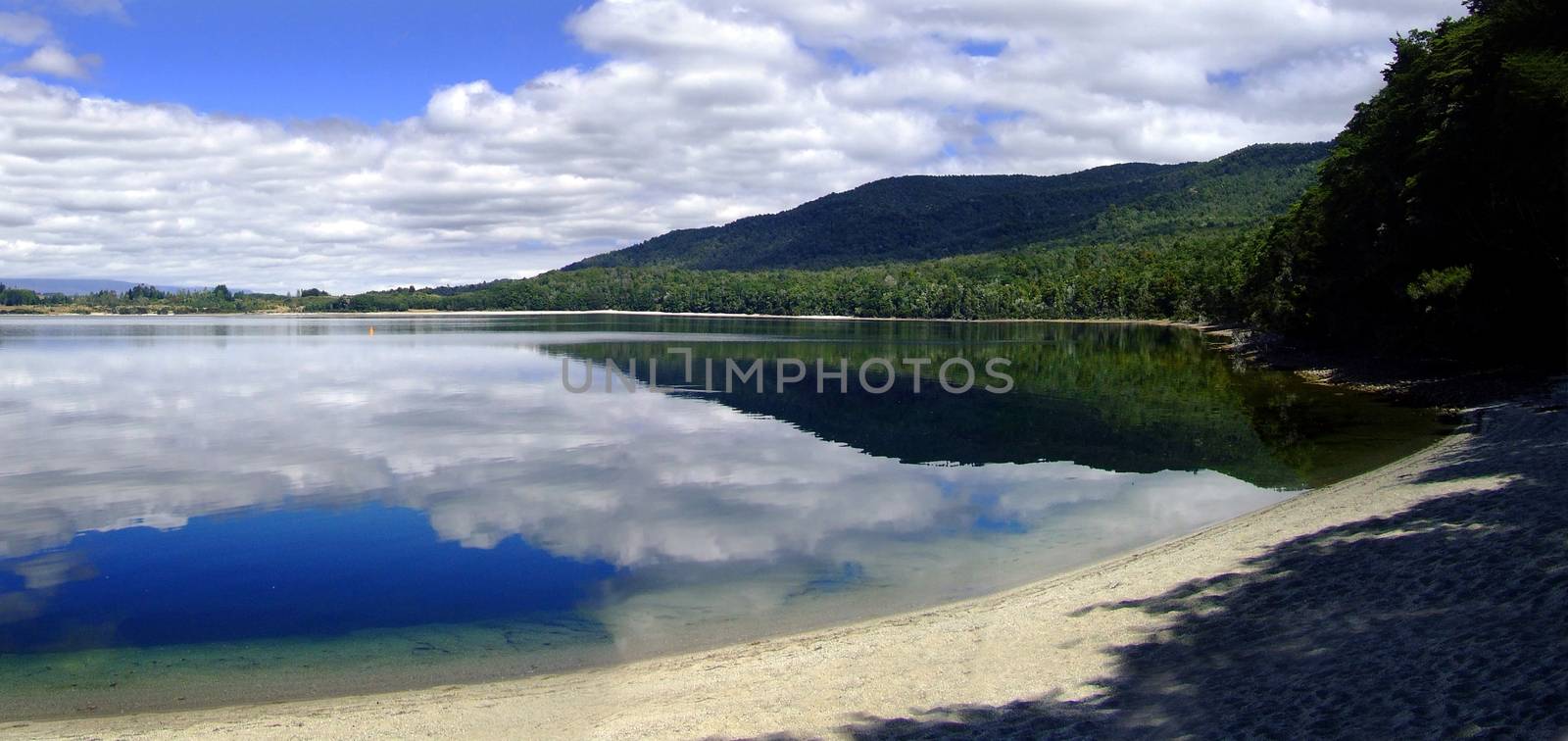 Lake Te Anau surface reflecting white clouds with blue sky and sandy beach. South island, New Zealand Kepler track by vladiczech