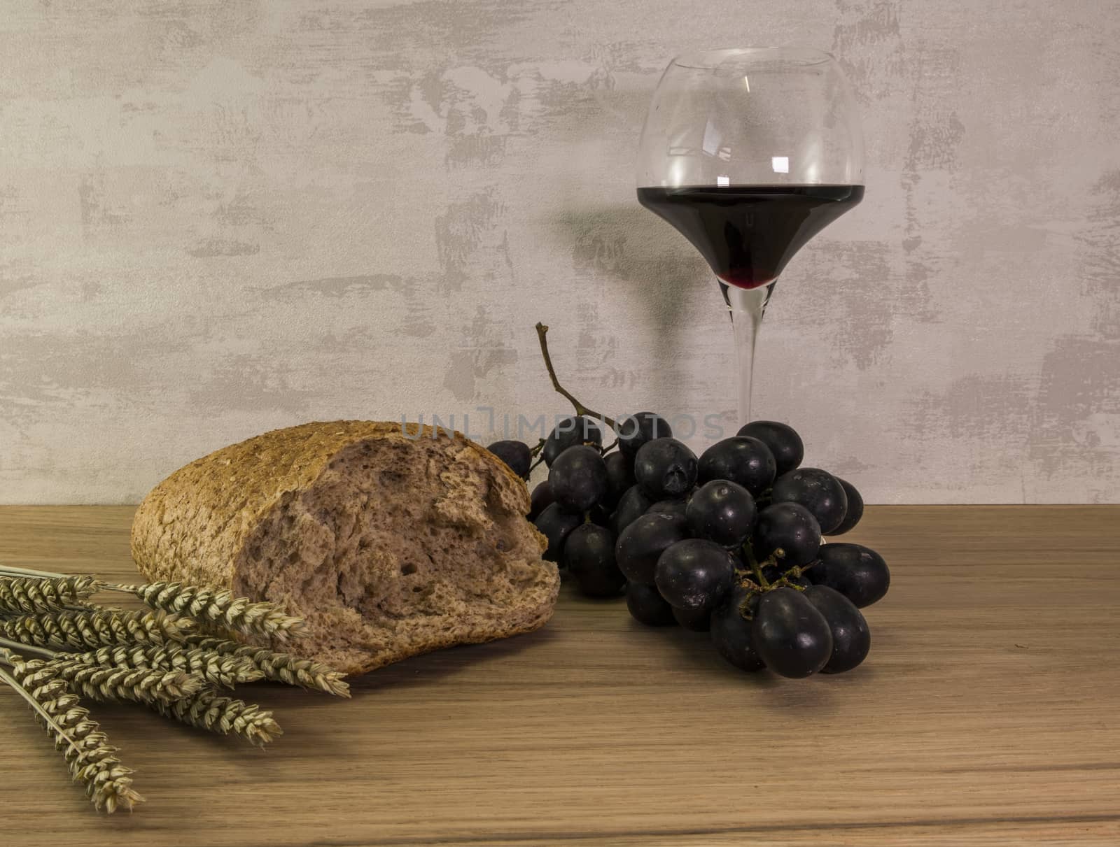 A wheat bread and shock of wheat with red grapes and glas of red wine as easter background