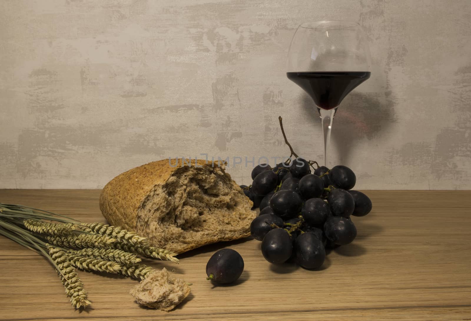 A wheat bread and shock of wheat with red grapes and glas of red wine as easter background