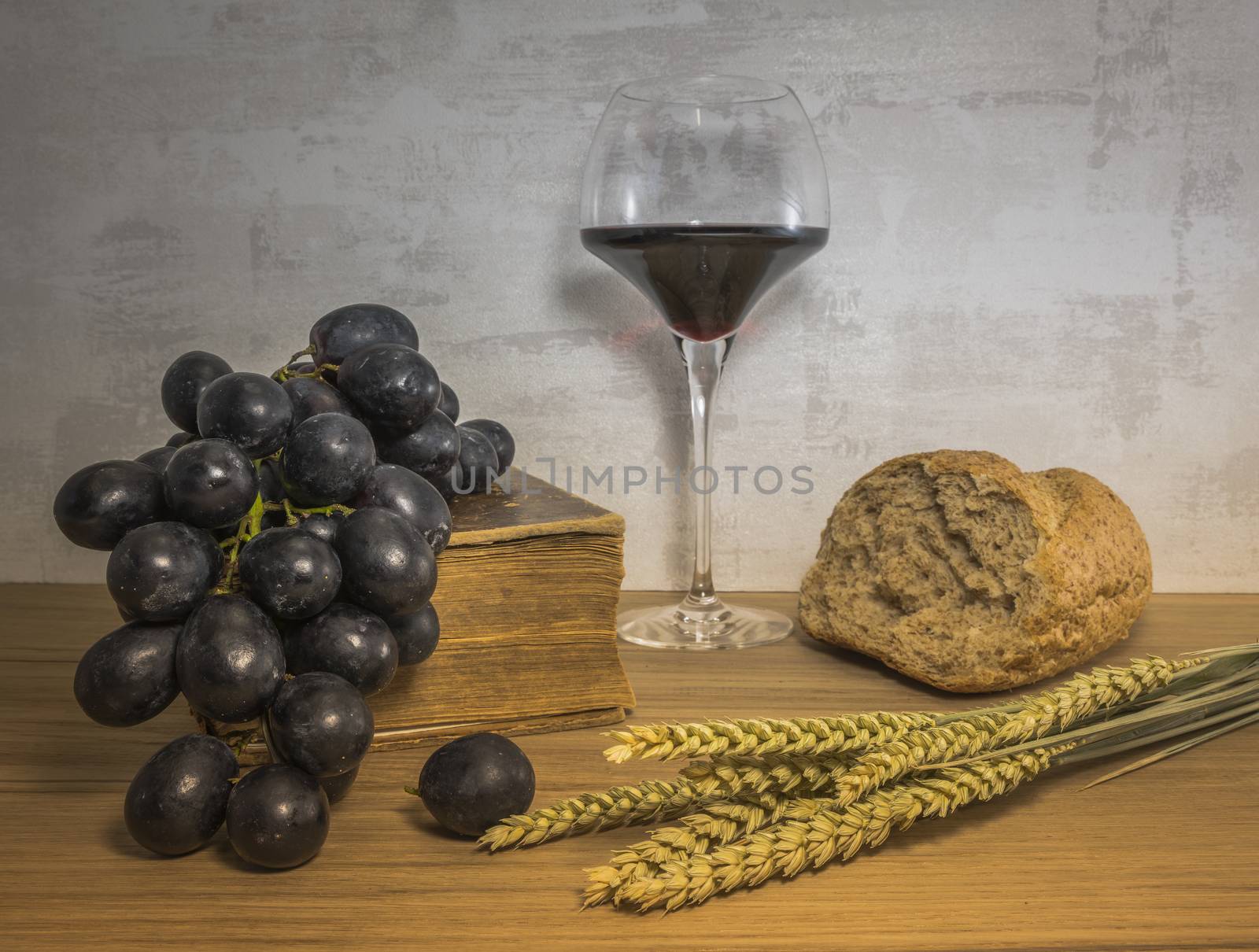 A wheat bread and shock of wheat with red grapes and glas of red wine and bible as easter background