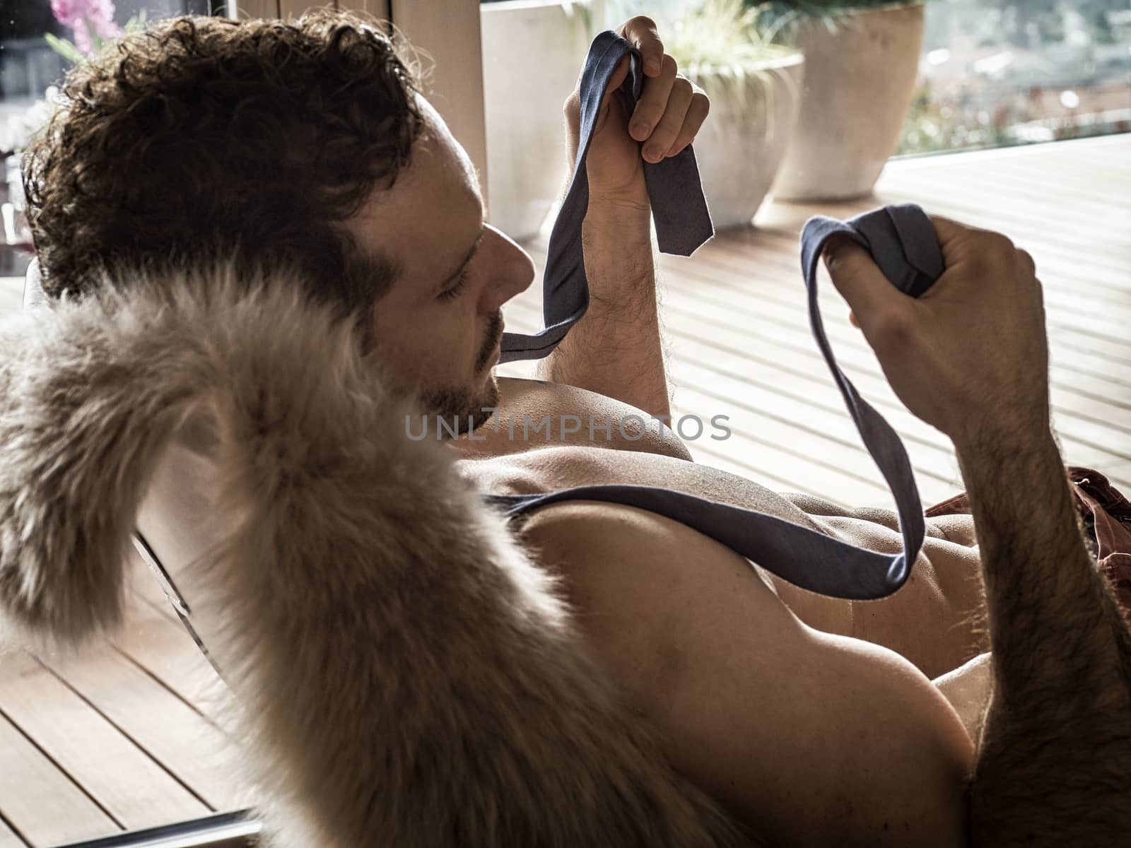 Shirtless sexy male model lying alone on couch in his living-room, looking away with a seductive attitude