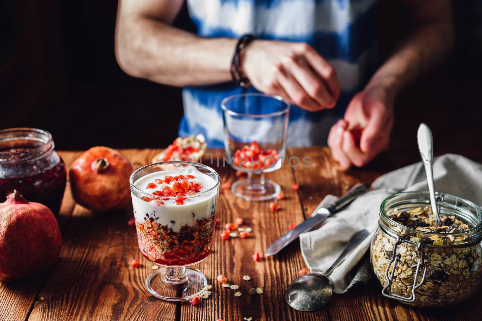 Dessert with Pomegranate and Man Prepare New Portion on Backdrop. Series on Prepare Healthy Dessert with Pomegranate, Granola, Cream and Jam