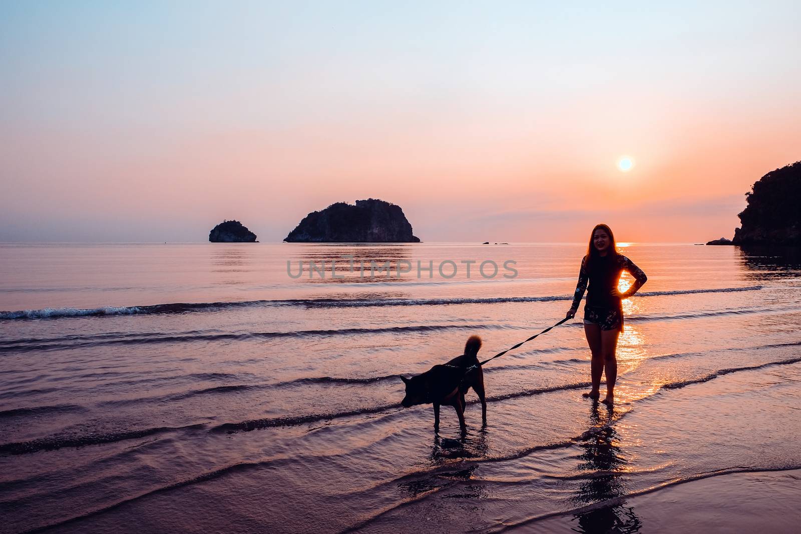 Woman and dog on beach at sunrise by ponsulak