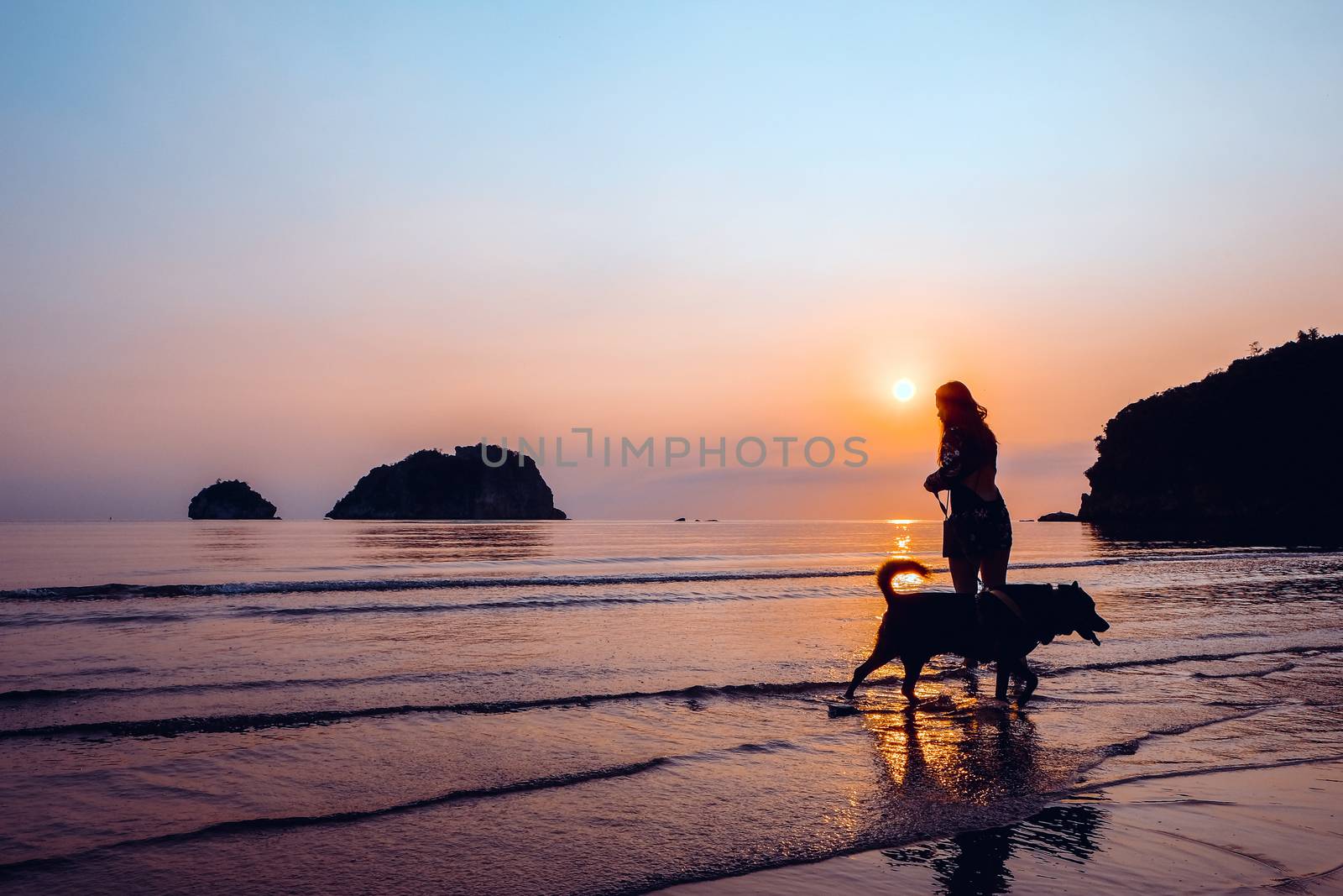 Woman and dog on beach at sunrise by ponsulak