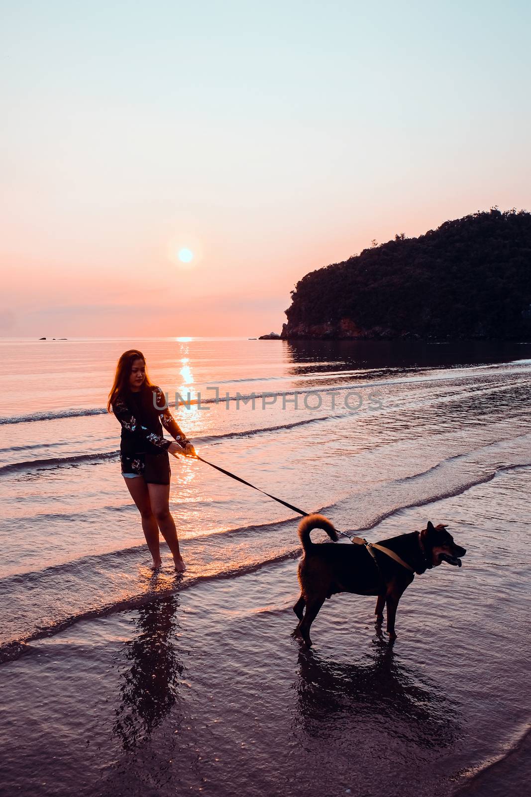 Woman and dog on beach at sunrise by ponsulak