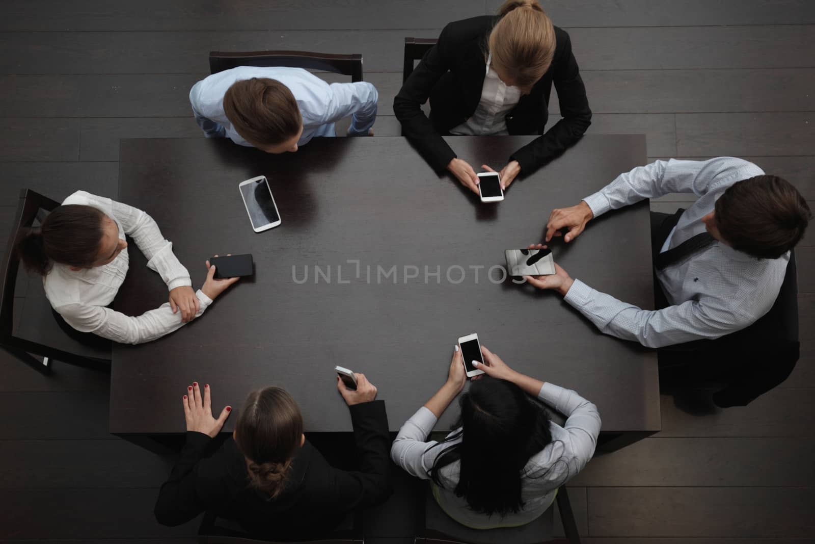 Business people with smartphones sitting around the table, top view