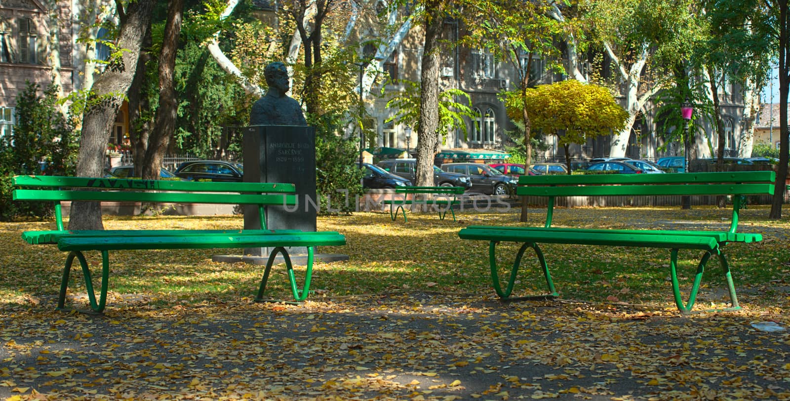 Park with two green benches, fallen leaves and monument at autumn time by sheriffkule