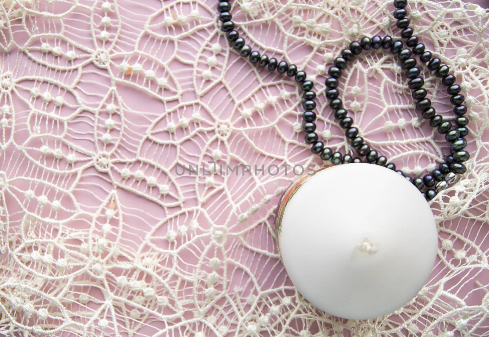 Flatlay pink background, graceful white expensive lace and elegant black pearl with candle, romantic style.