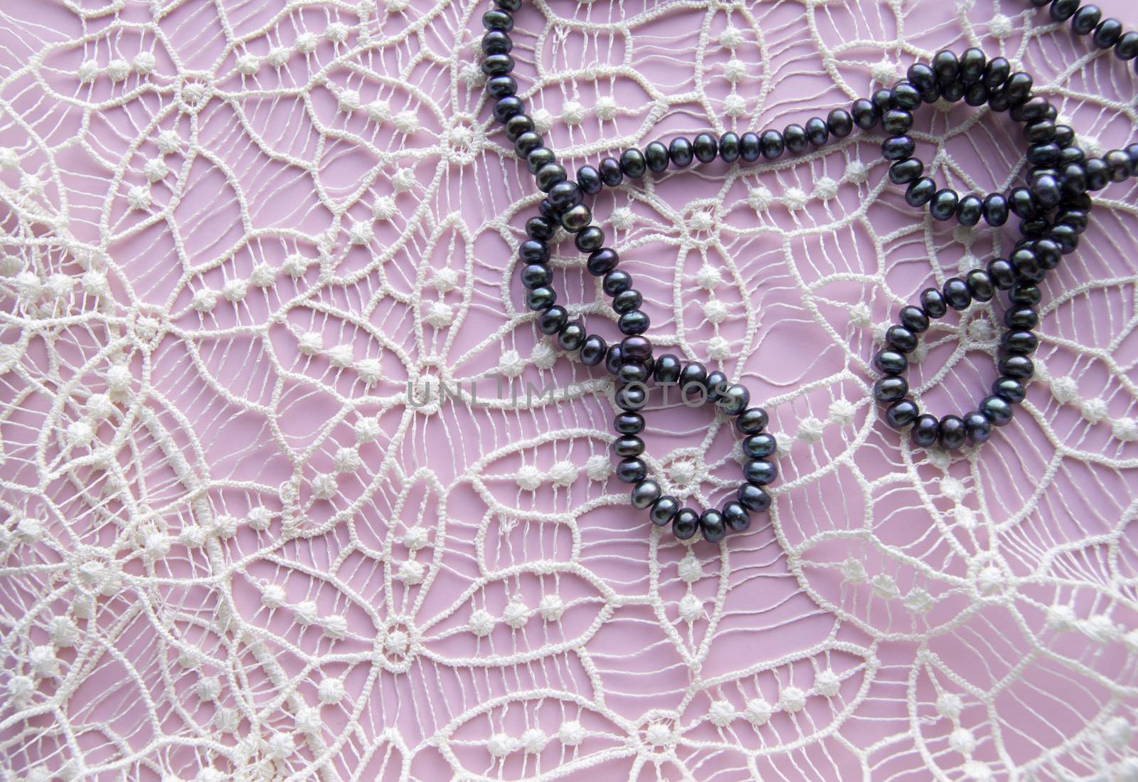 Lay Flat pink background and the gorgeous lace, glittering necklace of black pearls, and stylish bracelet. Beauty and fashion concept.