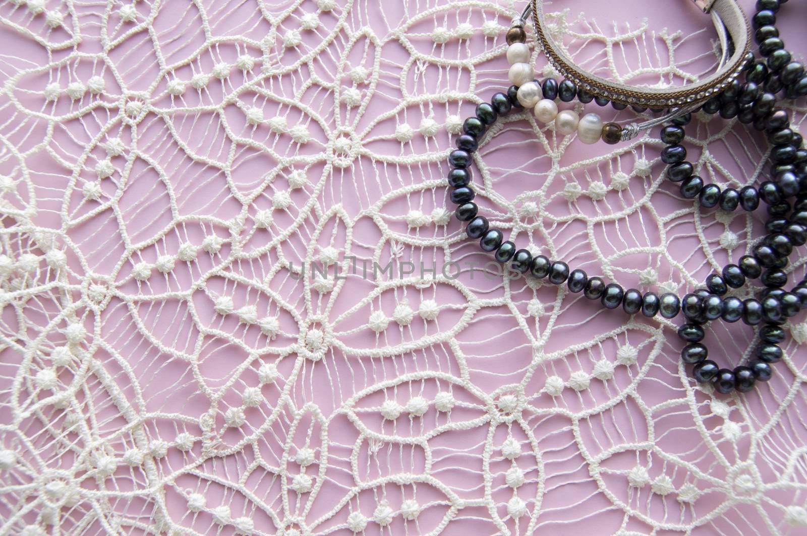 Lay Flat pink background and the gorgeous lace, glittering necklace of black pearls, and stylish bracelet. Beauty and fashion concept.