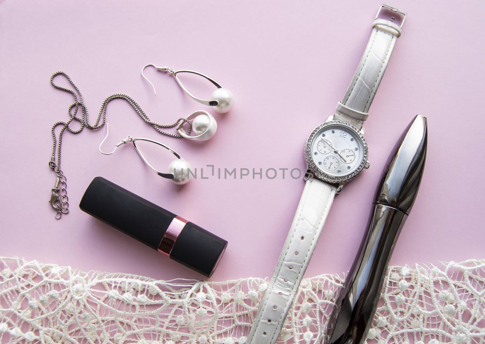 flat lay women's accessories collage with stylish watches, earrings and pendant with white pearls, lipstick, mascara on a Lacy pink background.