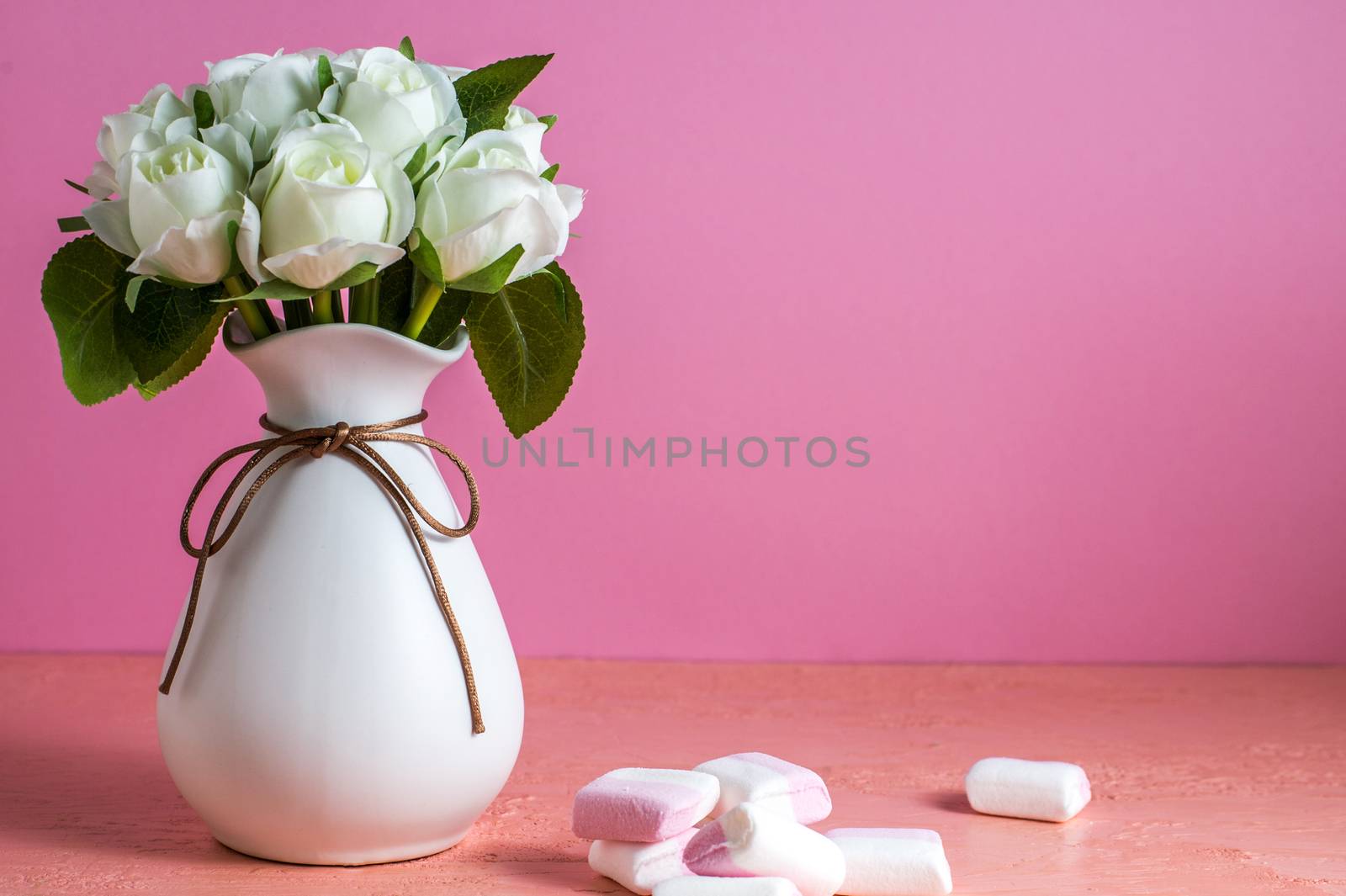 Copyspace with colorful mini marshmallows on a table next to white roses on a pink background