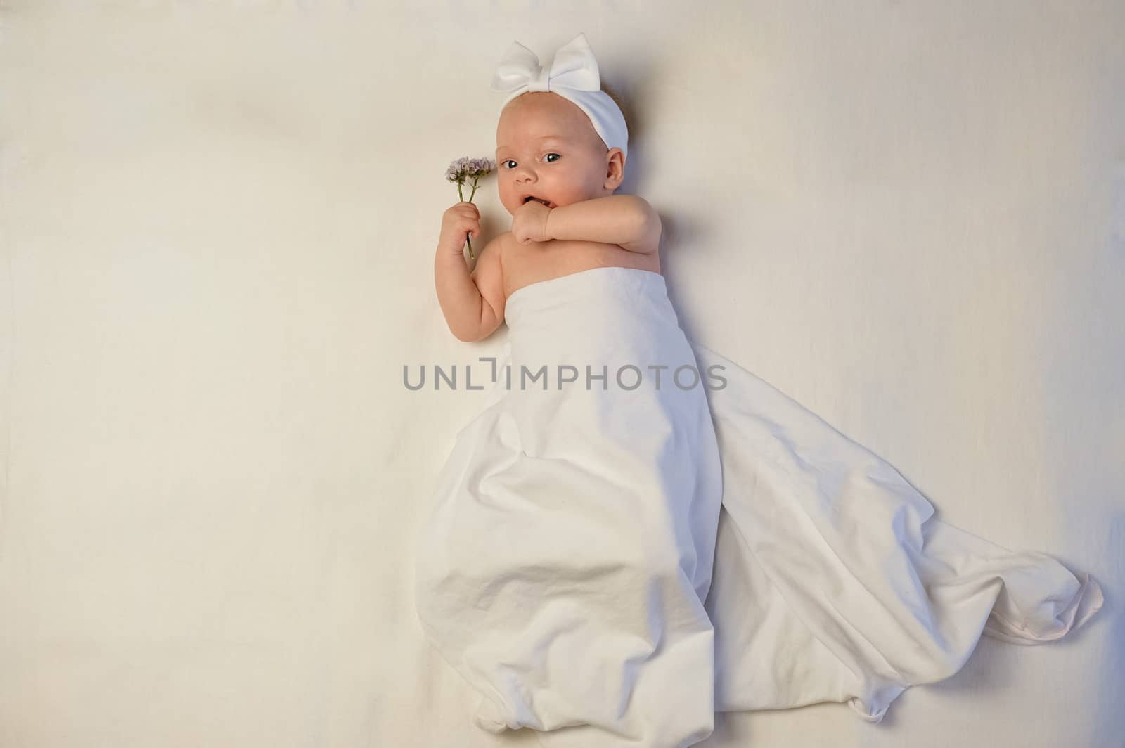 The baby girl with a bandage on his head holding a rose in his hand. The baby smiles.