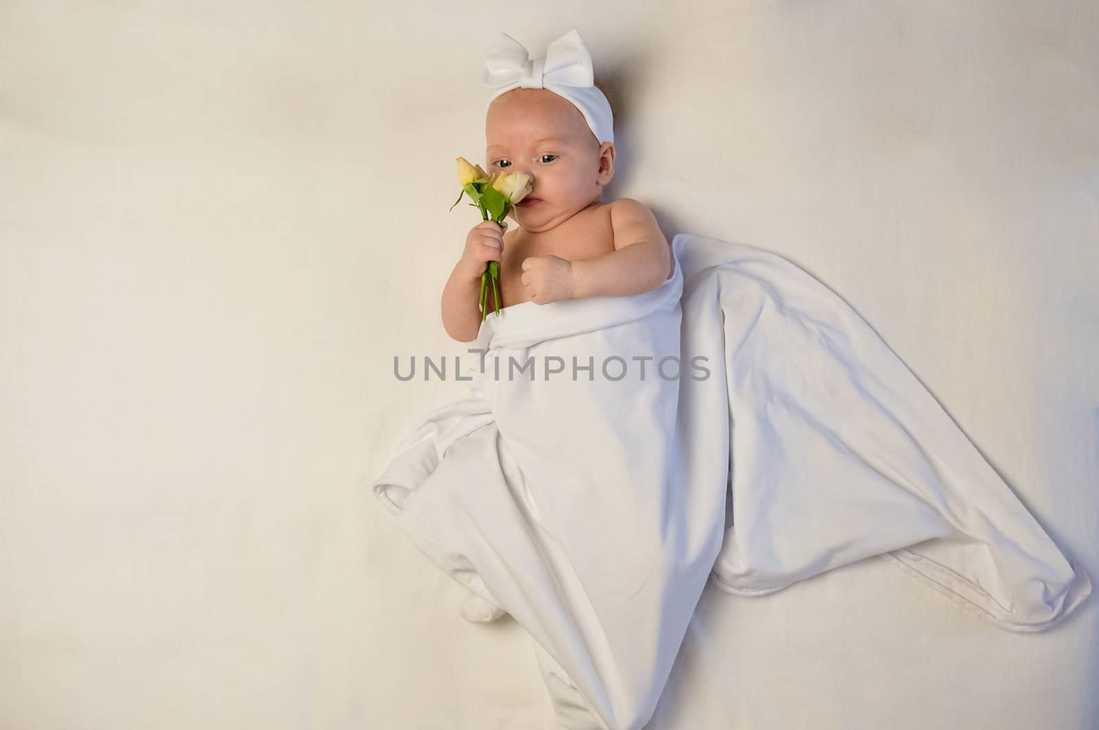 The baby girl with a bandage on his head holding a rose in his hand. The baby smiles.