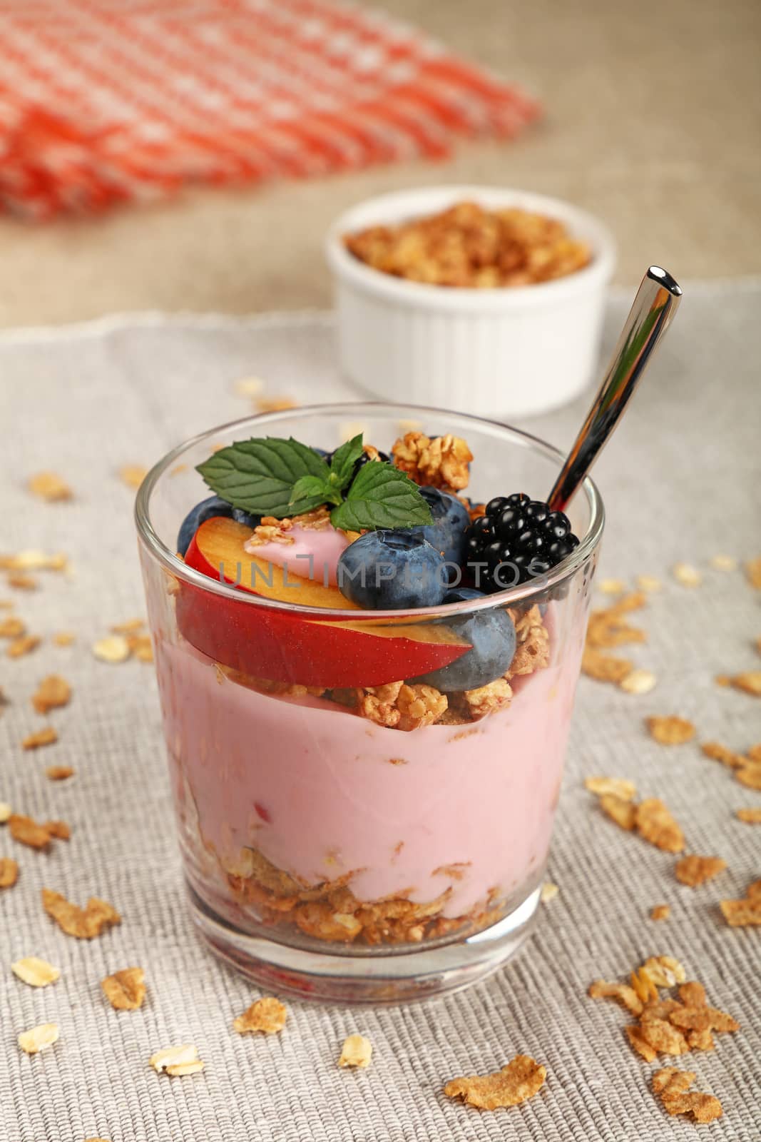 Close up portion of muesli granola breakfast with yogurt in glass, fruits and berries, high angle view