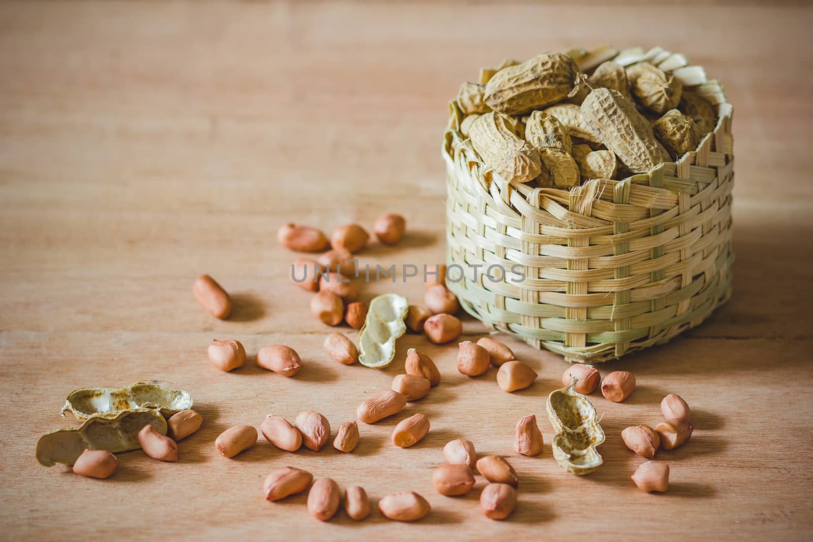 Peanuts in mini bamboo basket on brown wood background