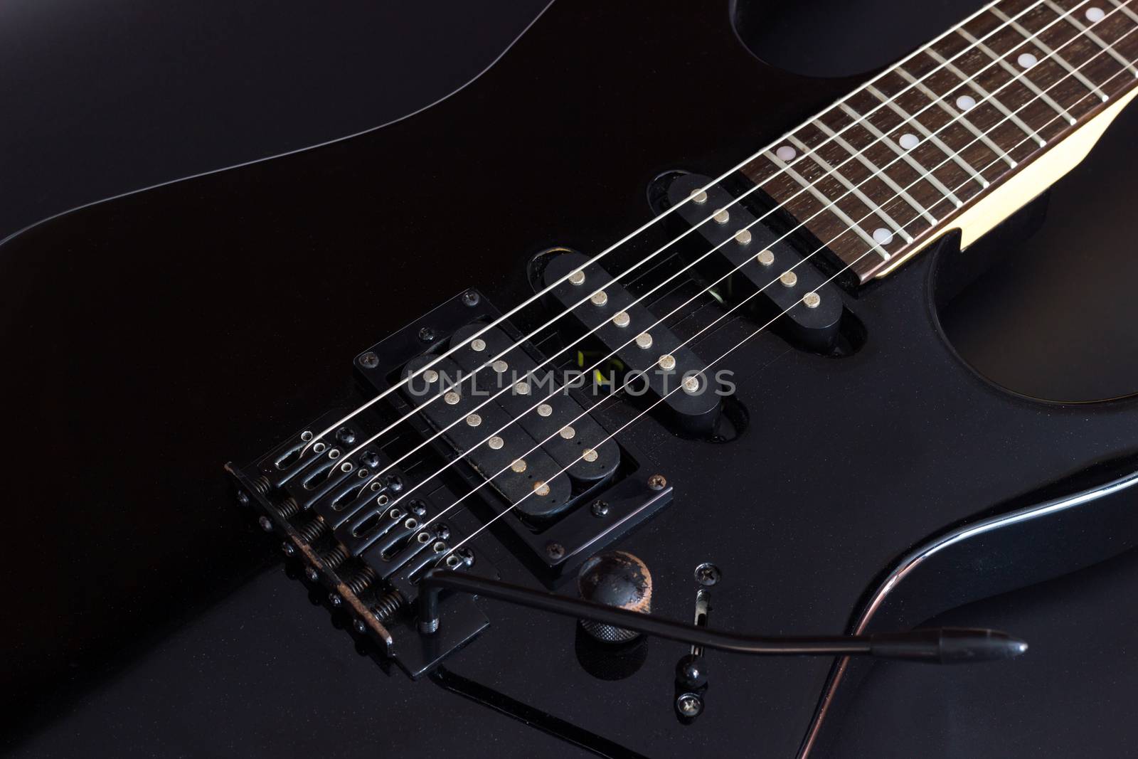 Black electric guitar on dark background.