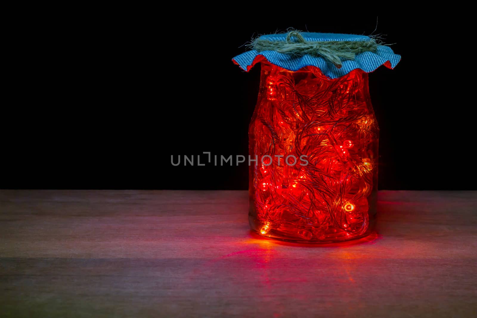 Red LED light in the glass bottle in darkness on brown wood table. Keep electrical energy for economical use. Concept of love the world and energy saving.