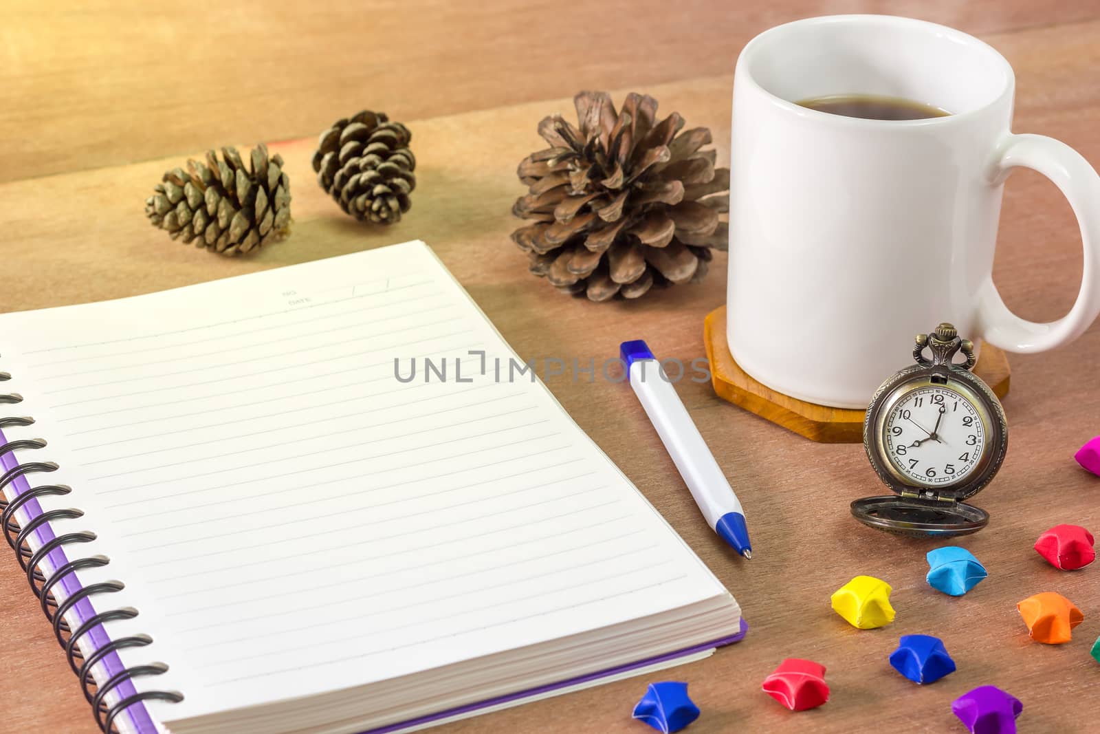 Black coffee with a notebook on a brown table. In the morning and Vintage clock at 8 o’clock. Paper stars and pine cones laid on wooden table.