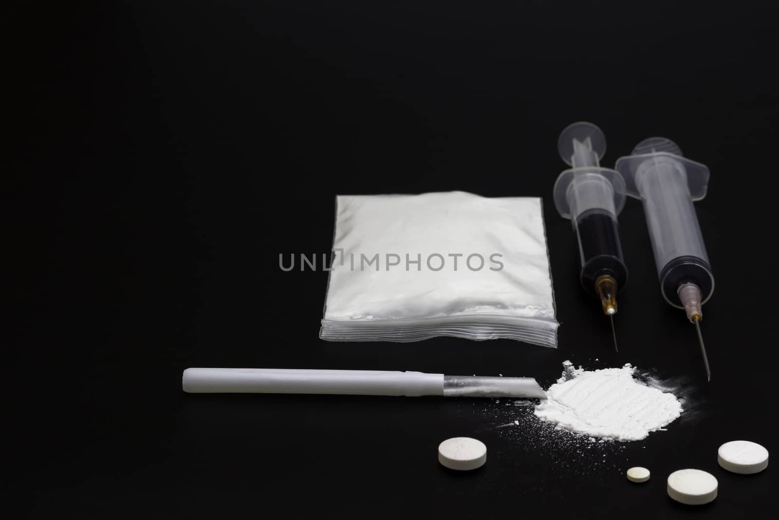 Fake Heroin or diacetylmorphine bag and syringes placed side by side. Low key addictive substance on darkness background.