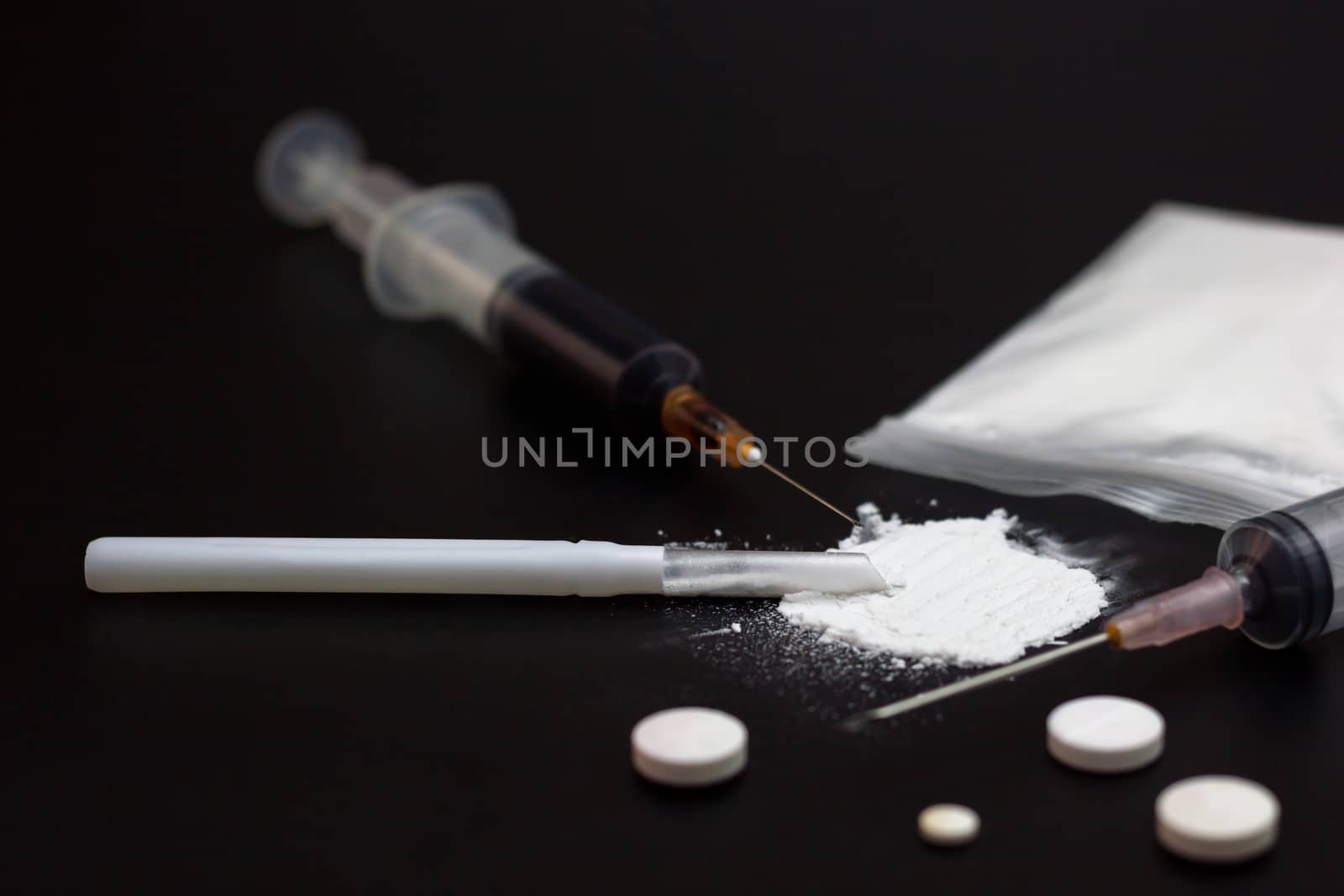 Fake Heroin or diacetylmorphine bag and syringes placed side by side. Low key addictive substance on darkness background.